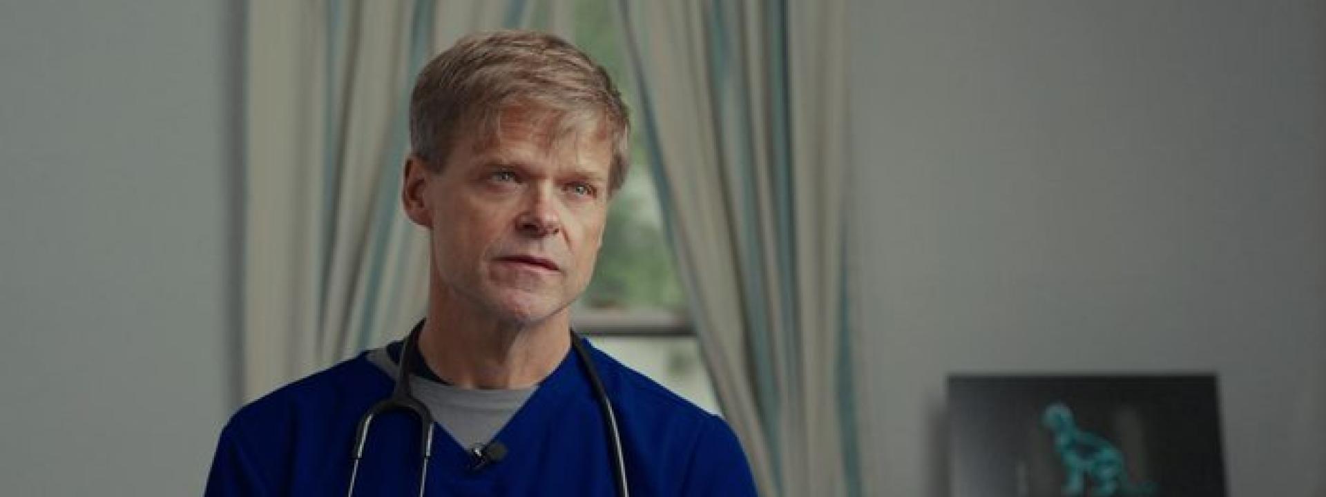 Dr. Reed Hall in blue scrubs with a stethoscope, talking about feline wellness exams